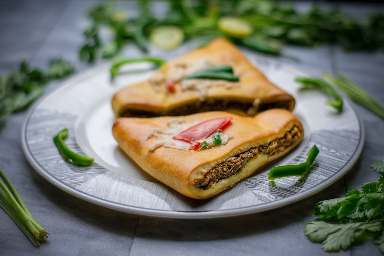 Tasty calzone served on an elegant plate with fresh green herbs in the background.