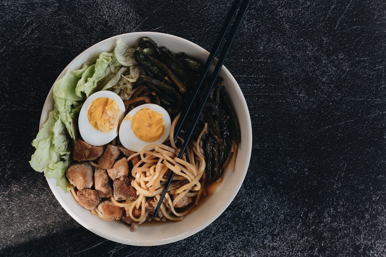 A vibrant ramen bowl with chopsticks, noodles, eggs, and vegetables, captured in a top view.